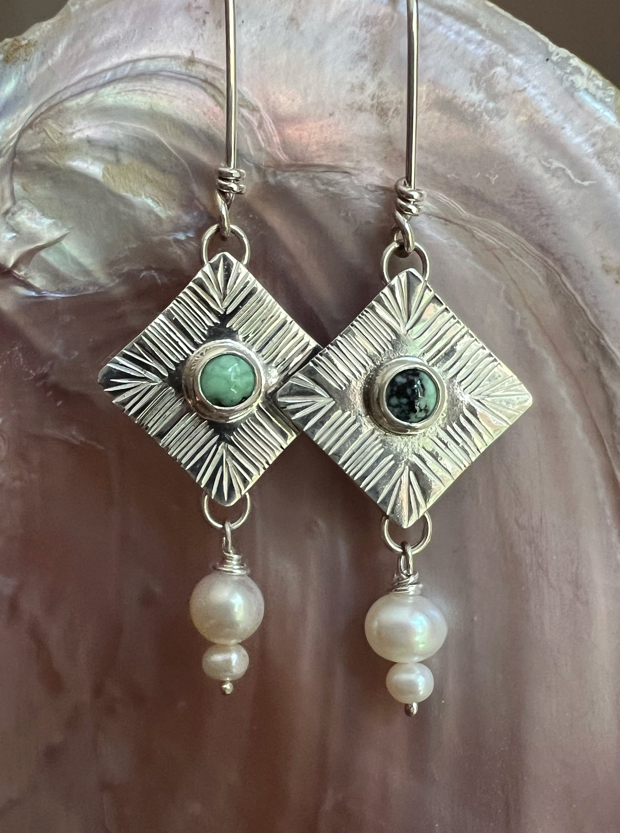 Silver earrings with green gemstones and pearl drops on a textured surface