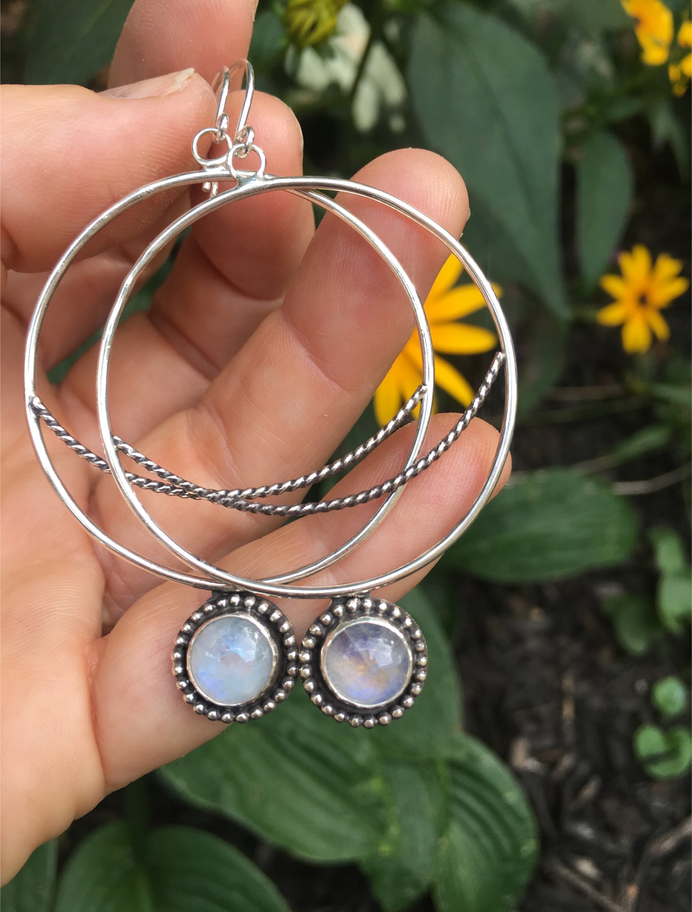 Crescent  Moon Hoops with Rainbow Moonstone Shown in Hand with Flowers in Background